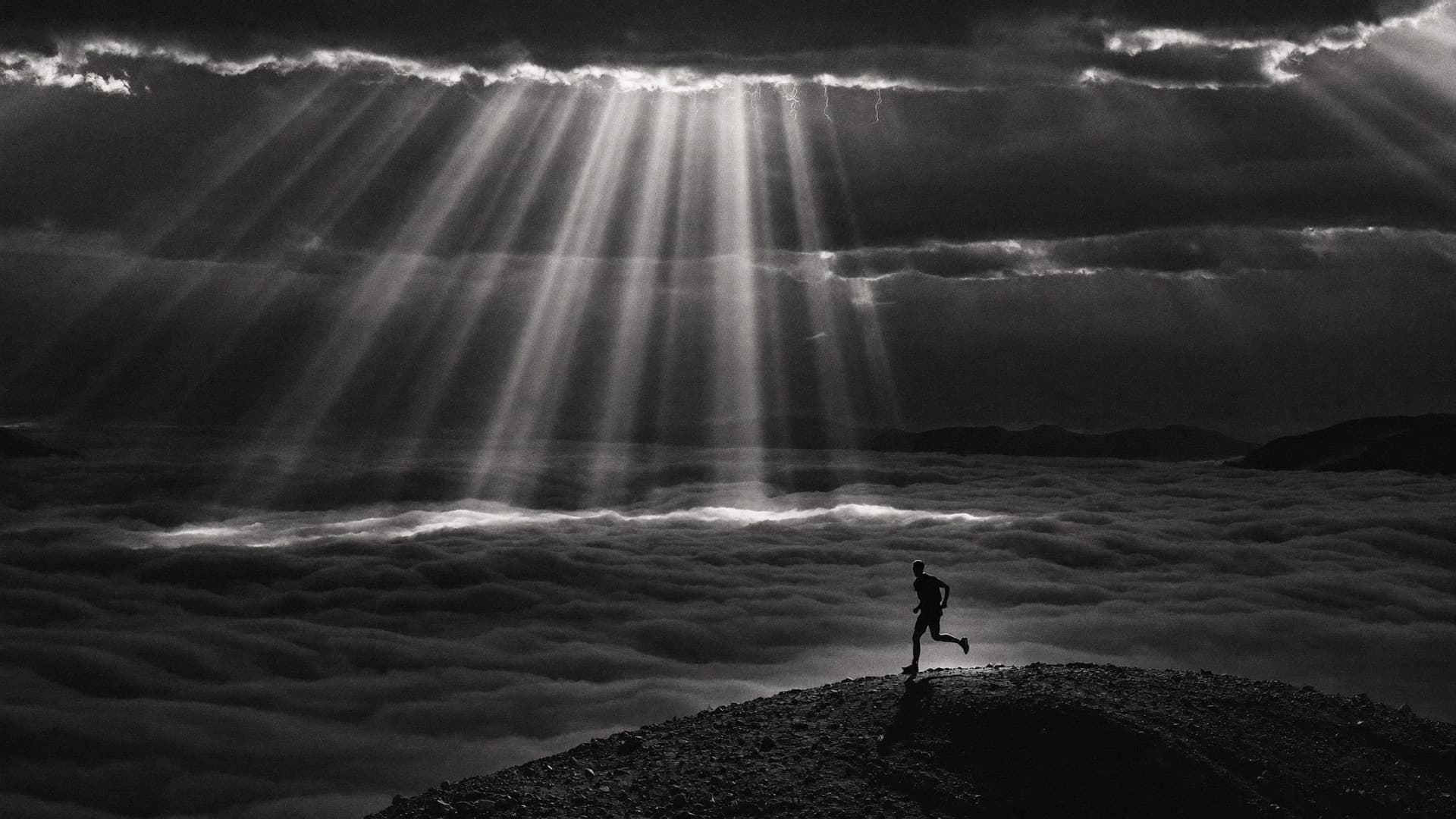 Runner above the clouds beneath breaking light